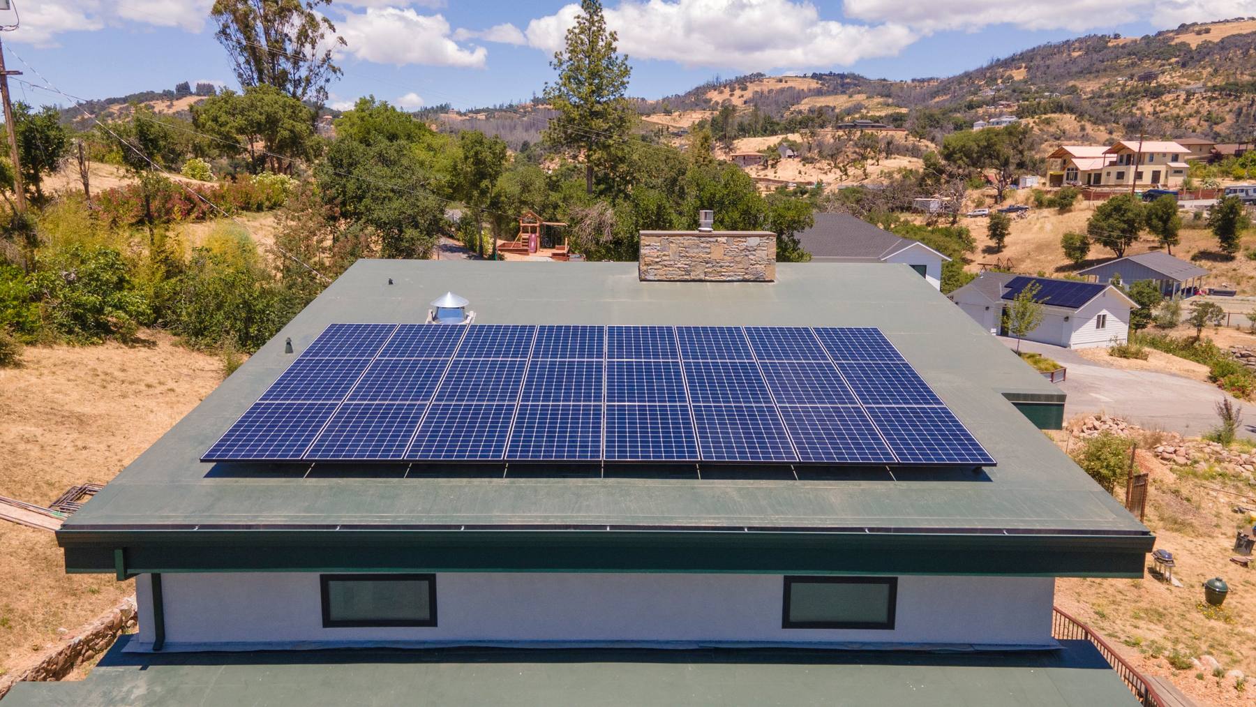 Aerial view of a flat-roof home with a rooftop solar array in the California foothills