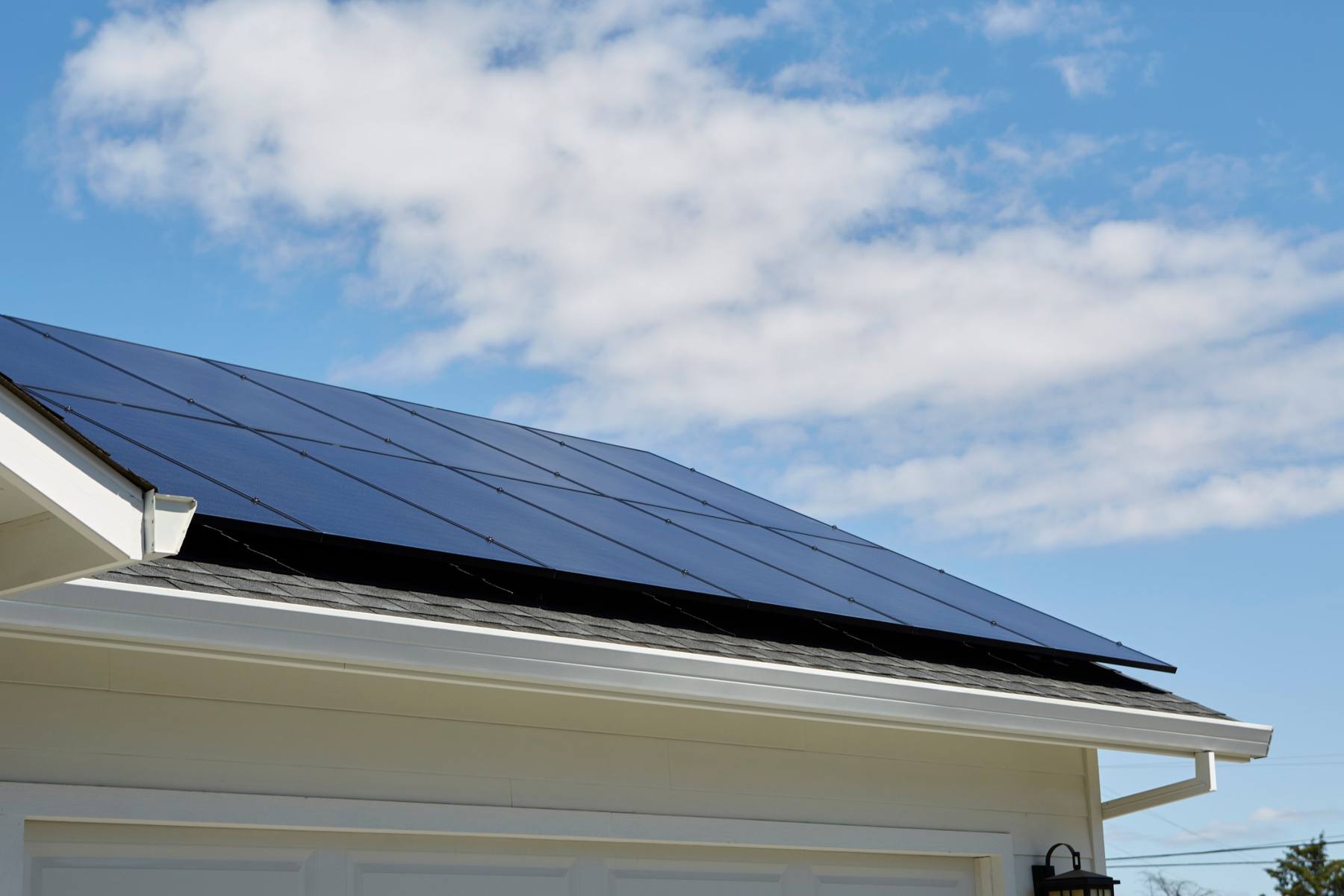 Close view of black solar panels on a shingle roof against a blue sky