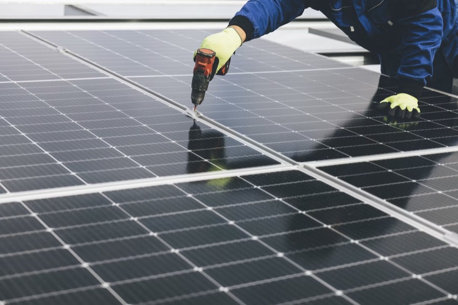 A solar installer fastening panels on a rooftop array
